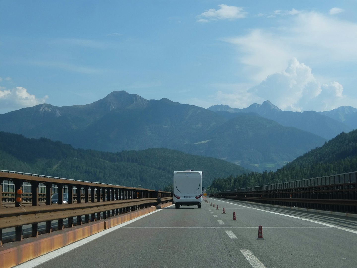White camper van driving along a highway toward distant mountains.
