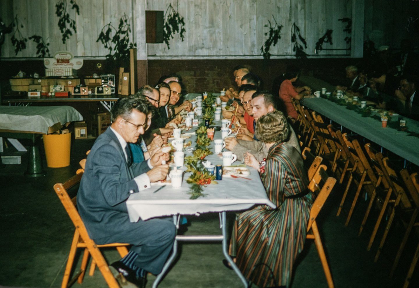 Diverse adults eating and socializing at community hall tables.